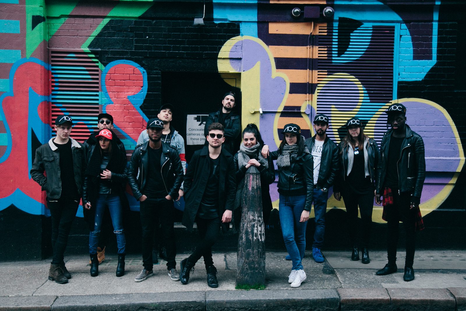 Full AOC crew posed together in front of a vibrant colourful mural